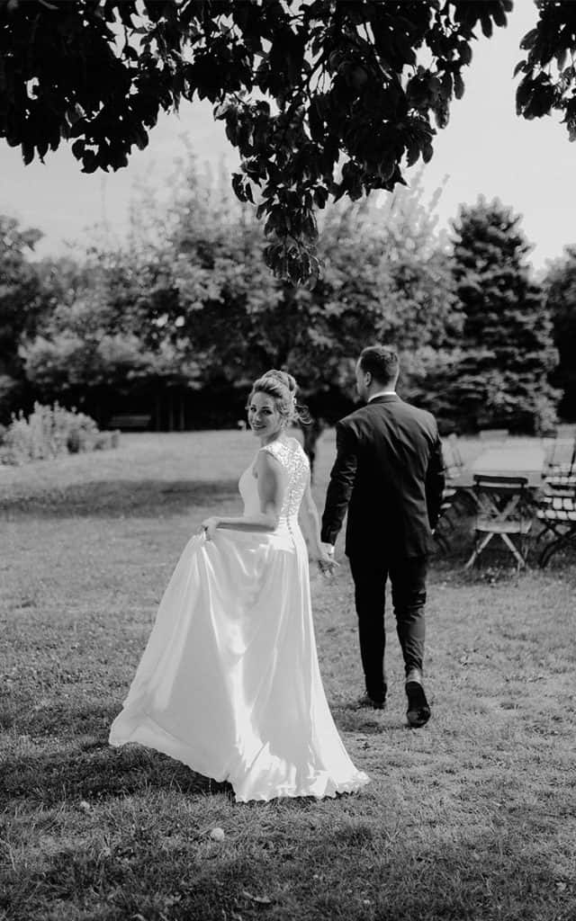 Braut mit einem Brautkleid mit Spitzenrücken läuft in einen Garten
