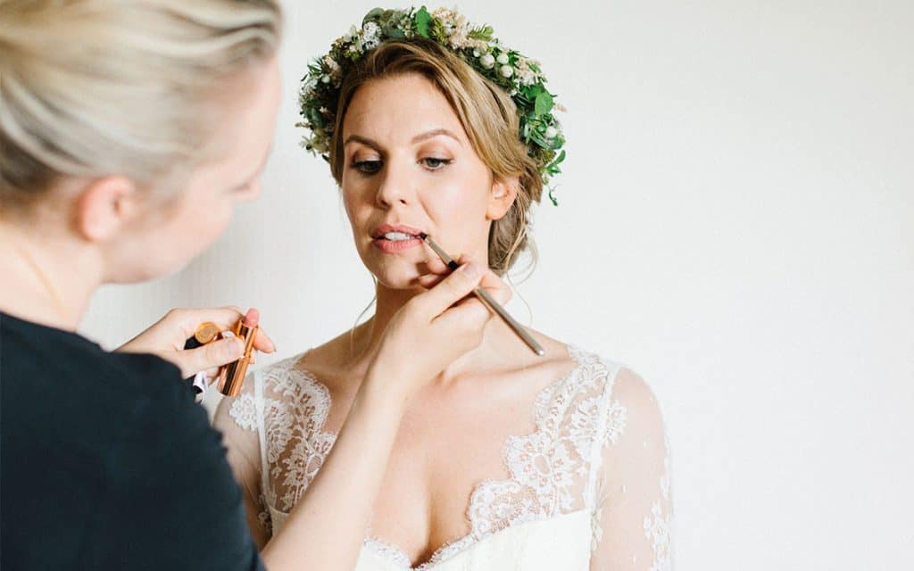 Visagistin frischt Lippenstift bei der Braut auf