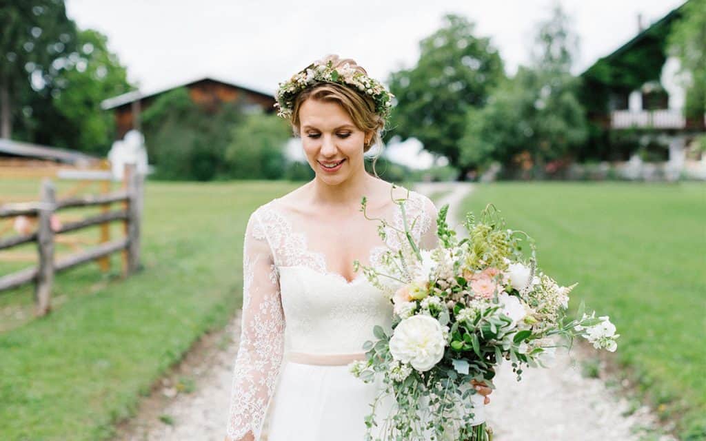 Braut mit Blumenkranz läuft vor einer Häuserreihe mit großem Blumenstrauss